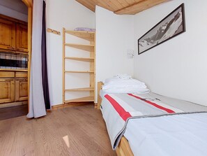A bedroom with a bunk bed, a single bed, wooden flooring, a kitchen area with wooden cabinets, and a framed picture on the wall. - Ginabelle 1 by Interhome (Chamonix)