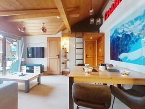 A cozy living space with a wooden ceiling, a dining table with chairs, a TV, and a large window. - Ginabelle 1 by Interhome (Chamonix)