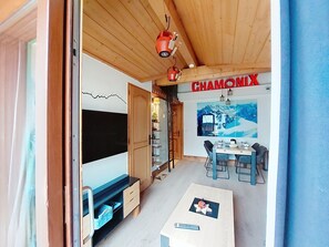 Een kamer met een houten plafond, een eethoek met een tafel en stoelen, een grote flatscreen-tv, en een bordje met de tekst 'CHAMONIX'.
