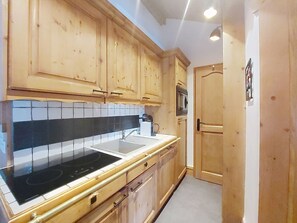 A compact kitchen with wooden cabinets, a black stove, and a white sink. - Ginabelle 1 by Interhome (Chamonix)