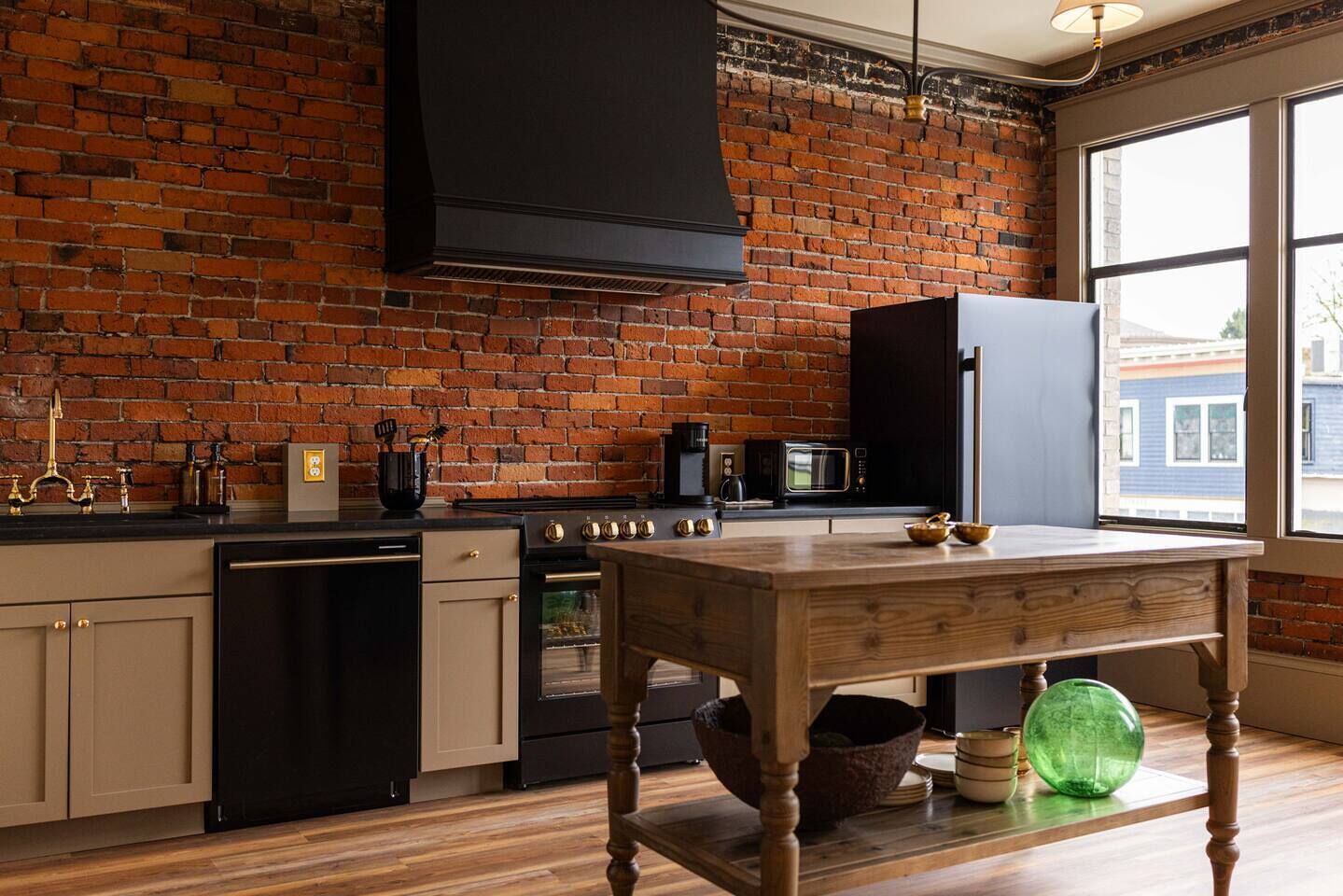 Una cocina con pared de ladrillo, mesa de madera y electrodomésticos modernos.
