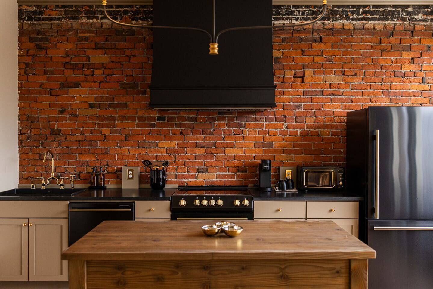 Une cuisine avec un mur en briques, une table en bois et des appareils électroménagers modernes.