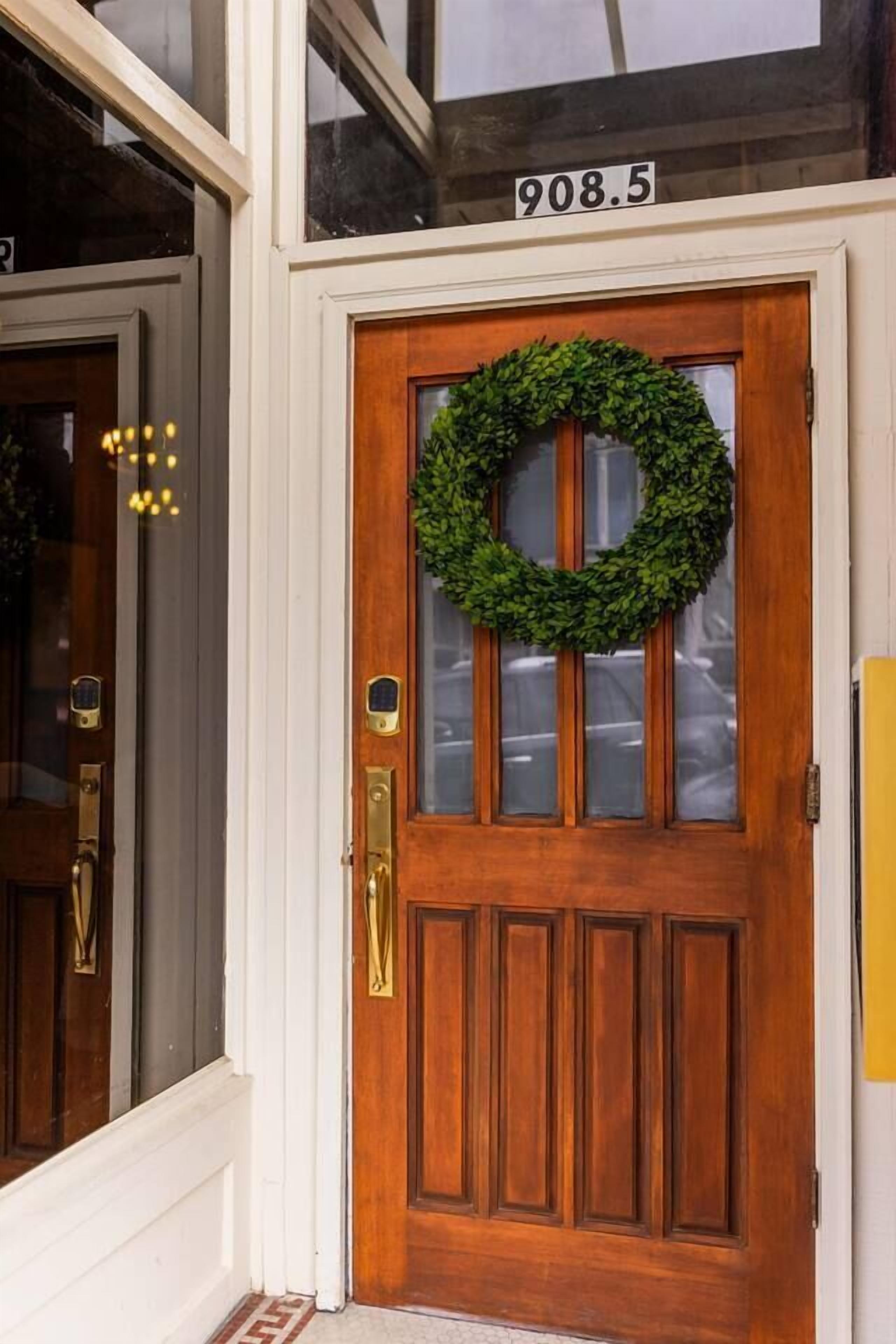 A wooden door with a green wreath, a number plaque, and a brass doorbell.