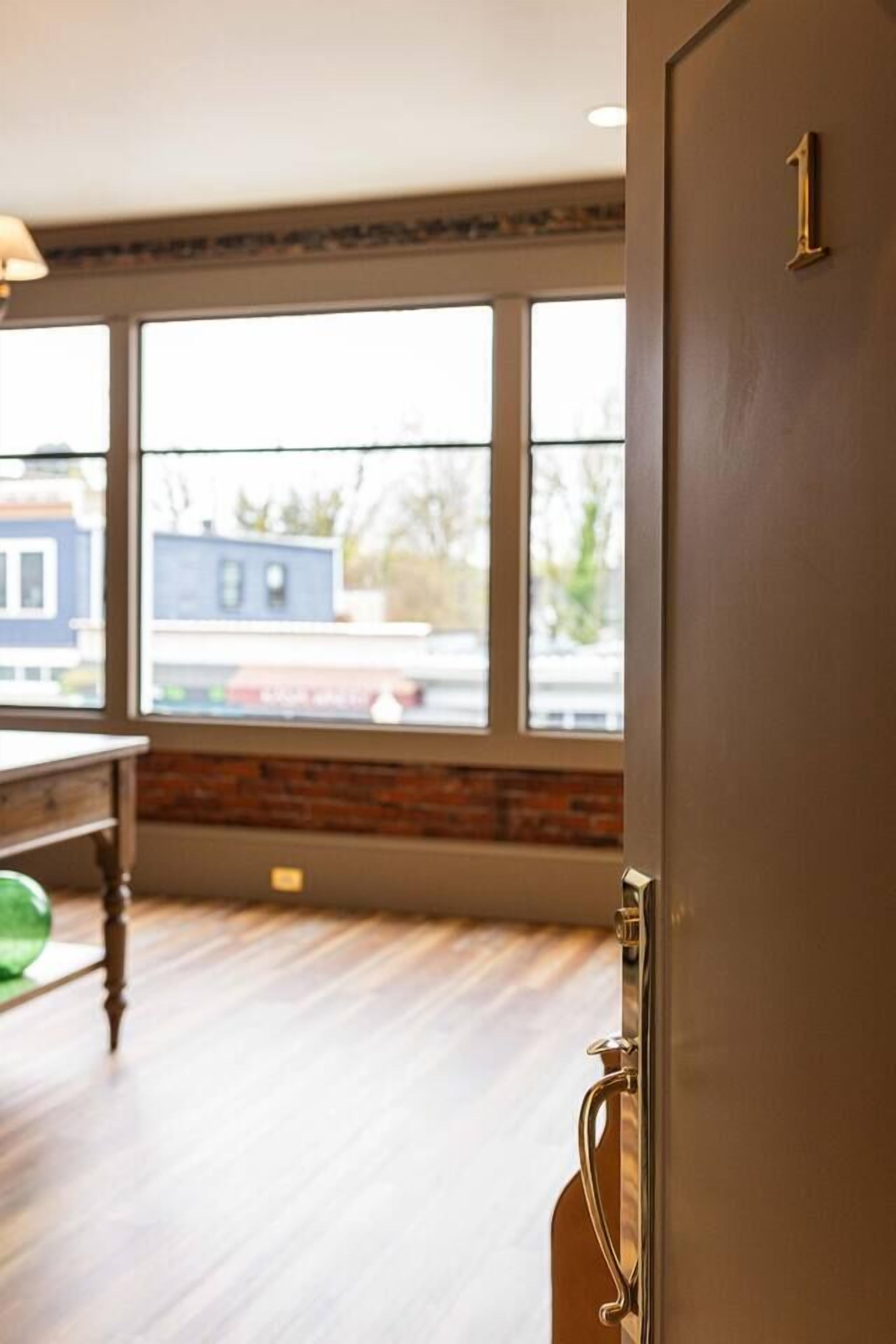 Una habitación con un ventanal grande, suelo de madera y una puerta con un número.