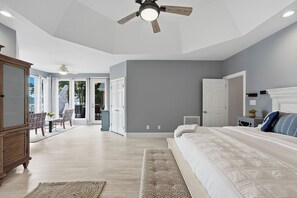 Ein Schlafzimmer mit einem Bett, einem Deckenventilator, einem Schminktisch und Blick ins Freie durch eine Tür.