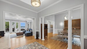 A spacious living area with a wooden floor, a sofa, a dining table with chairs, and a kitchen area with wooden cabinets. - Lakefront + Private Dock | Hot Tub + Pool Table + Cabana | Point of View (Mooresville)