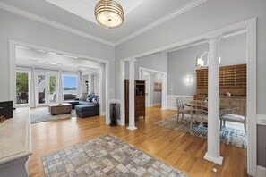 A spacious living area with a wooden floor, a sofa, a dining table with chairs, and a kitchen area with wooden cabinets. - Lakefront + Private Dock | Hot Tub + Pool Table + Cabana | Point of View (Mooresville)