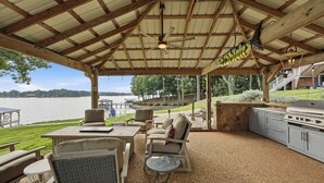 An outdoor patio with a covered area, seating, a grill, and a view of a lake. - Lakefront + Private Dock | Hot Tub + Pool Table + Cabana | Point of View (Mooresville)