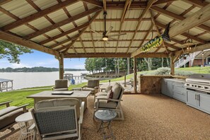 An outdoor patio with a covered area, seating, a grill, and a view of a lake. - Lakefront + Private Dock | Hot Tub + Pool Table + Cabana | Point of View (Mooresville)