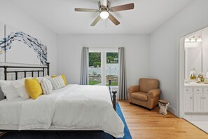 Een slaapkamer met een bed, een stoel, een badkamer met een spiegel en uitzicht op de omgeving.