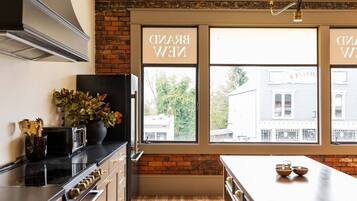 A kitchen with a brick wall, a large window, and a countertop with a plant and kitchenware.
