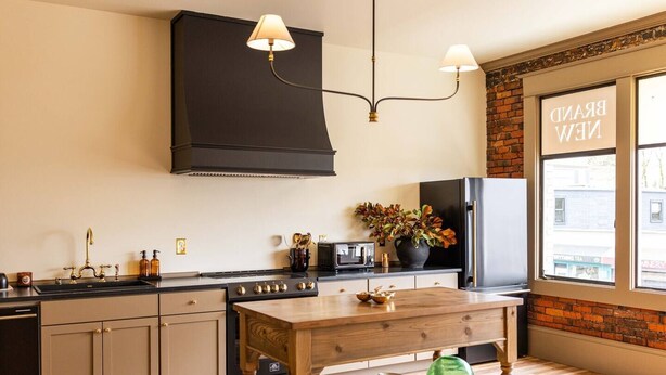 Une cuisine moderne dotée d’un îlot central, d’une hotte noire et offrant une vue sur un bâtiment en briques à l’extérieur.