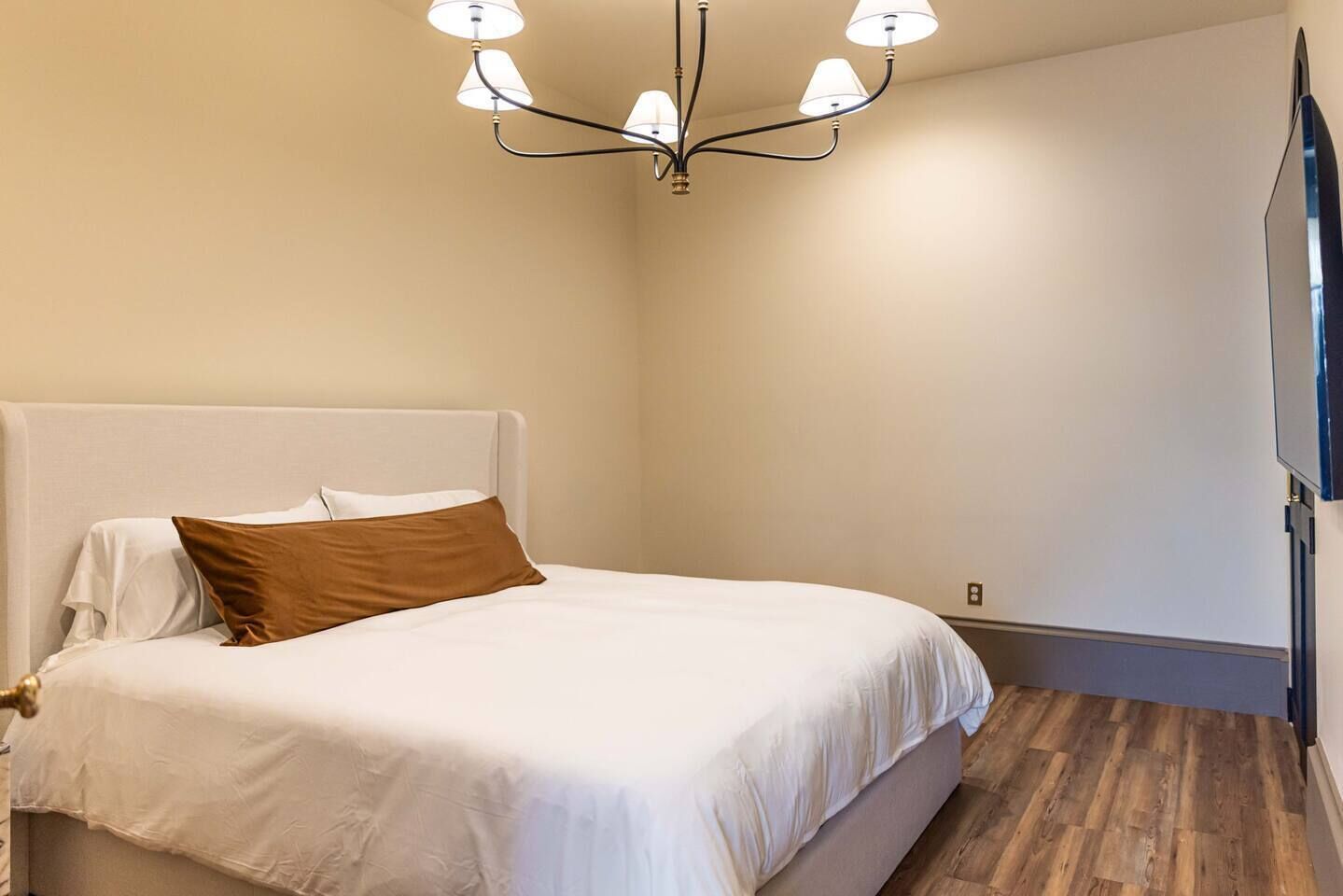 A bedroom with a bed, a chandelier, and a wooden floor.