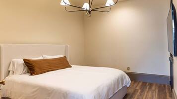 A bedroom with a bed, a chandelier, and a wooden floor.