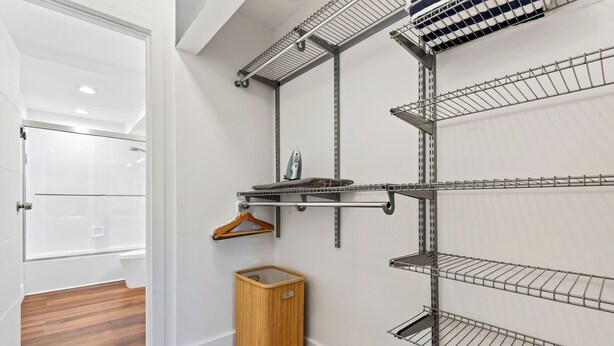 A walk-in closet with metal shelving units, a wooden basket, and a hanging rack. - Garden Balcony + Pool + Deck | Walk to Beach + Dining | Skyline & Salt (Sunny Isles Beach)