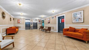 A lobby with a reception desk, two elevators, and a seating area with orange sofas and chairs. - Garden Balcony + Pool + Deck | Walk to Beach + Dining | Skyline & Salt (Sunny Isles Beach)