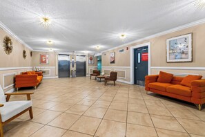 Eine Lobby mit einer Rezeption, zwei Aufzügen und einer Sitzecke mit orangefarbenen Sofas und Sesseln.
