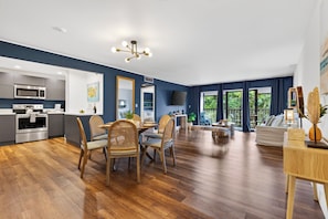 A modern kitchen with built-in appliances, a dining area with wooden chairs, and a living room with a large window. - Garden Balcony + Pool + Deck | Walk to Beach + Dining | Skyline & Salt (Sunny Isles Beach)