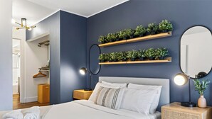 A modern bedroom with a bed, bedside lamps, a mirror, and wall-mounted plant shelves. - Garden Balcony + Pool + Deck | Walk to Beach + Dining | Skyline & Salt (Sunny Isles Beach)