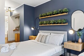 Ein modernes Schlafzimmer mit Bett, Nachttischlampen, einem Spiegel und Wandregalen für Pflanzen.