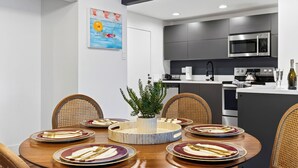 A modern kitchen with a microwave, oven, and a dining area with a round table set for six. - Garden Balcony + Pool + Deck | Walk to Beach + Dining | Skyline & Salt (Sunny Isles Beach)
