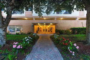 A hotel entrance with a paved pathway leading to the door, surrounded by flower beds with pink and red flowers. - Sunny Isles Condo • Shared Pool + Private Balcony • Near Beaches | Isle Vista (Sunny Isles Beach)