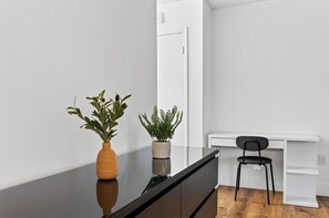Ein modernes Zimmer mit Holzboden, einem schwarzen Schreibtisch, einem weißen Stuhl und zwei Blumentöpfen.