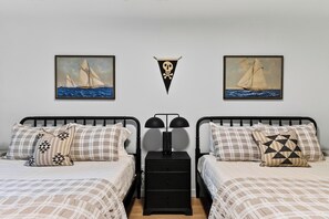 A room with two beds, each with a headboard, a nightstand with a lamp, and two framed paintings of sailboats on the wall. - Cannon Beach Stay + Treetop Deck + Walk To Beach + Haystack Rock | Salt & Spruce (Cannon Beach)
