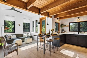 A modern kitchen with a wooden ceiling, large windows, and a dining area with stools. - Cannon Beach Stay + Treetop Deck + Walk To Beach + Haystack Rock | Salt & Spruce (Cannon Beach)
