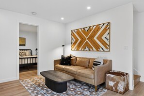 A modern living room with a leather sofa, a coffee table, and a patterned rug. - Cannon Beach Stay + Treetop Deck + Walk To Beach + Haystack Rock | Salt & Spruce (Cannon Beach)