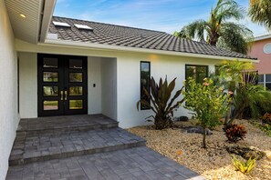 A modern house with a tiled roof, a black front door with glass panels, and a small front garden with pebbles and plants. - Waterfall Pool + Kayaks + Quick Gulf Access | Latitude 26° Luxury Retreat (Fort Myers)