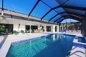 A swimming pool with clear blue water, surrounded by lounge chairs and a covered patio area. - Waterfall Pool + Kayaks + Quick Gulf Access | Latitude 26° Luxury Retreat (Fort Myers)