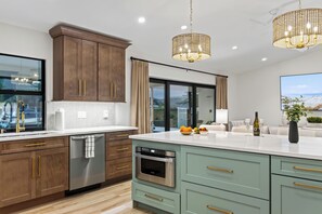 A modern kitchen with wooden cabinets, stainless steel appliances, and a large island with a built-in oven. - Waterfall Pool + Kayaks + Quick Gulf Access | Latitude 26° Luxury Retreat (Fort Myers)