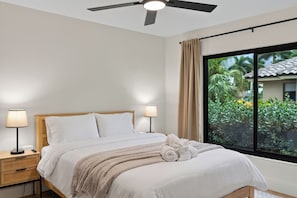 A hotel room with a bed, bedside lamps, a ceiling fan, and a window with a view of greenery. - Waterfall Pool + Kayaks + Quick Gulf Access | Latitude 26° Luxury Retreat (Fort Myers)