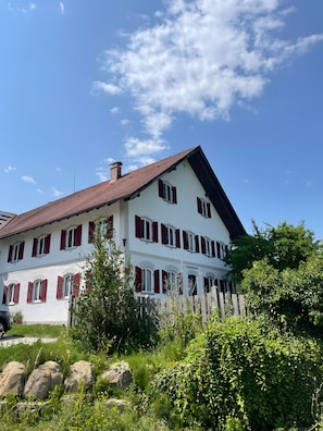 A two-story building with a red-tiled roof and white walls, surrounded by greenery and rocks. - Farmhouse 'Hohe Bleick' with Mountain View, Private Terrace and Wi-Fi (Wildsteig)