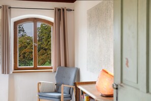 Een kamer met een raam, een stoel, een tafel en een lamp.