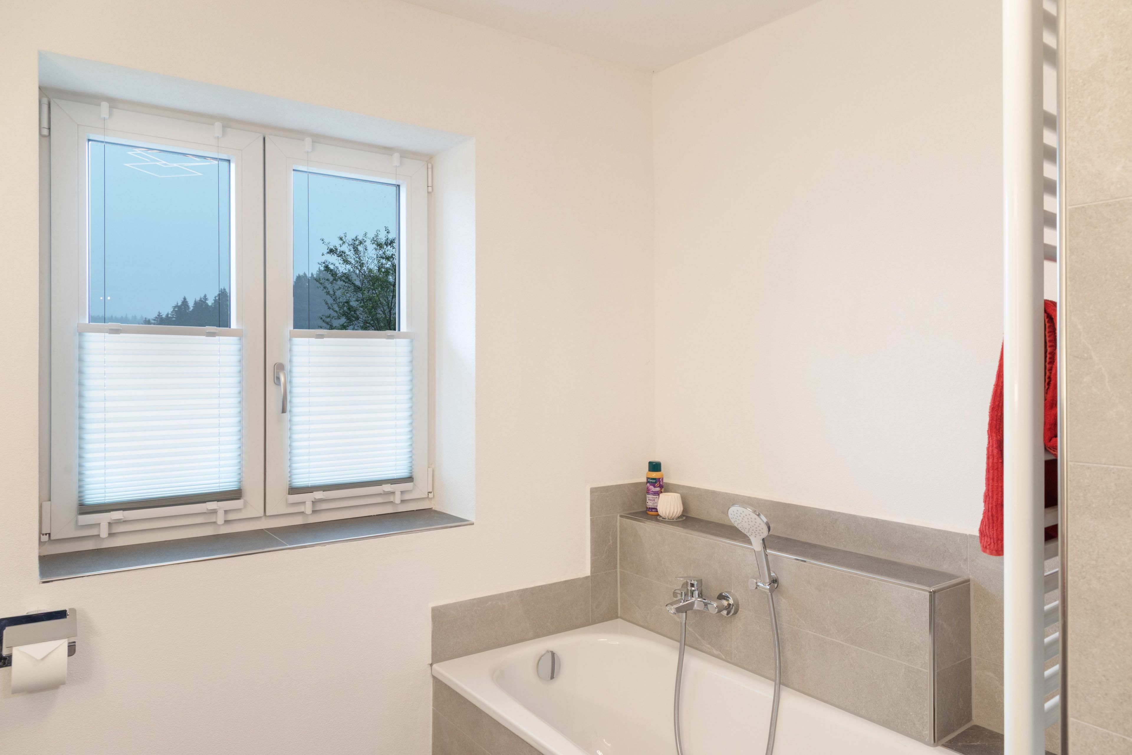 Ein Badezimmer mit Badewanne, einem Fenster mit Jalousien und einem Handtuchhalter.