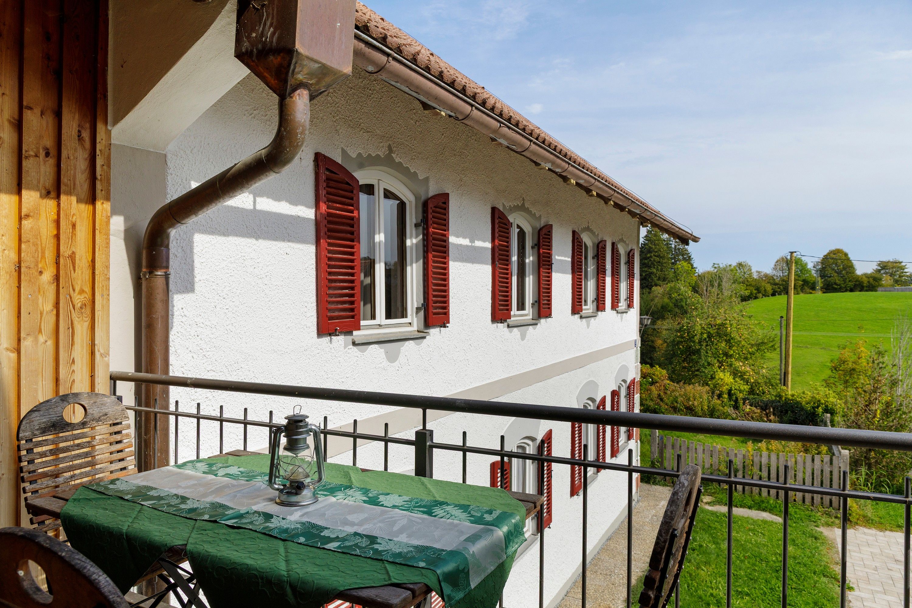 A balcony with a table, a lantern, and a view of a green field.
