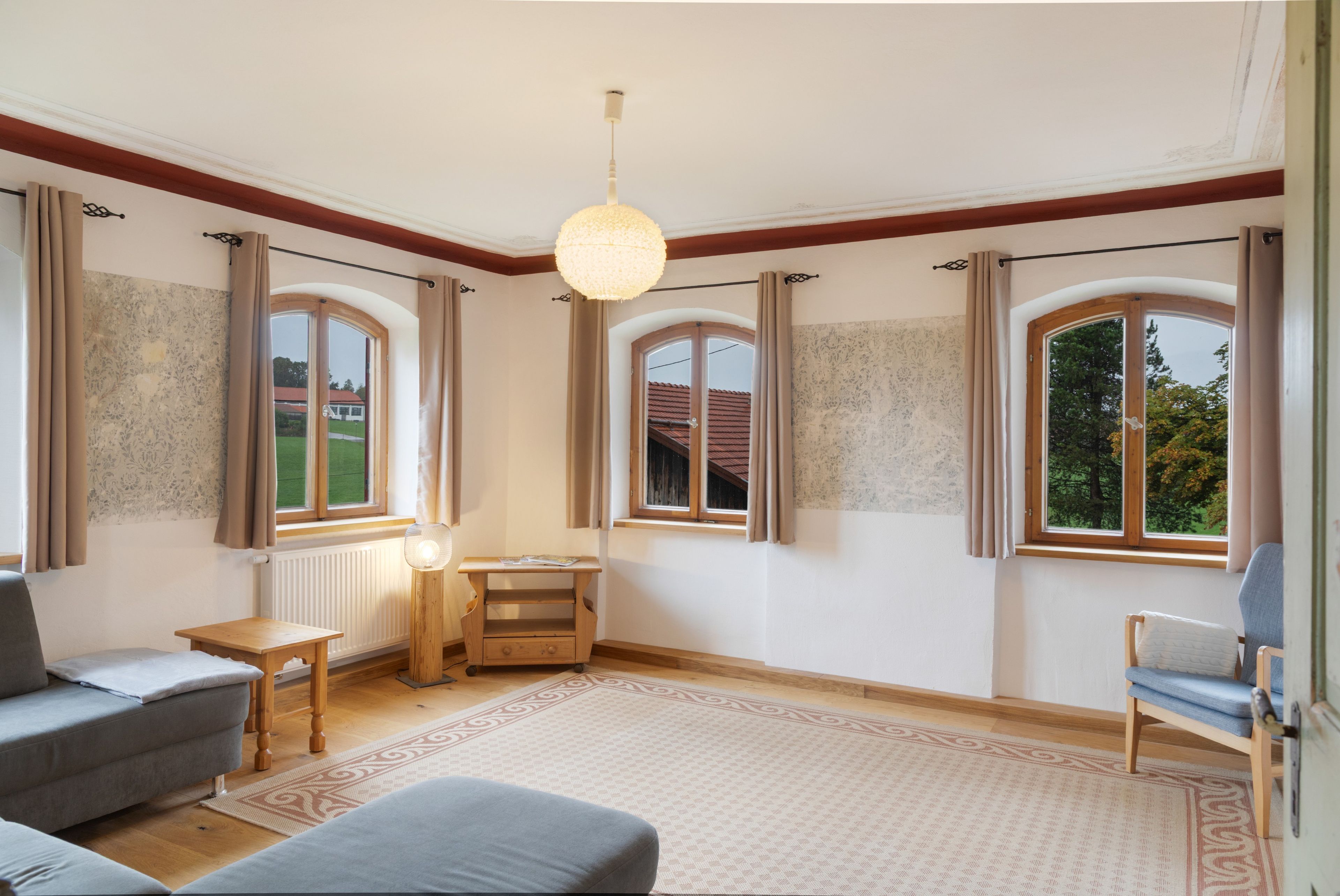 Um quarto espaçoso com uma grande janela, uma mesa de madeira, um sofá e uma cadeira.