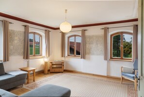 Ein geräumiger Raum mit großem Fenster, einem Holztisch, einer Couch und einem Sessel.