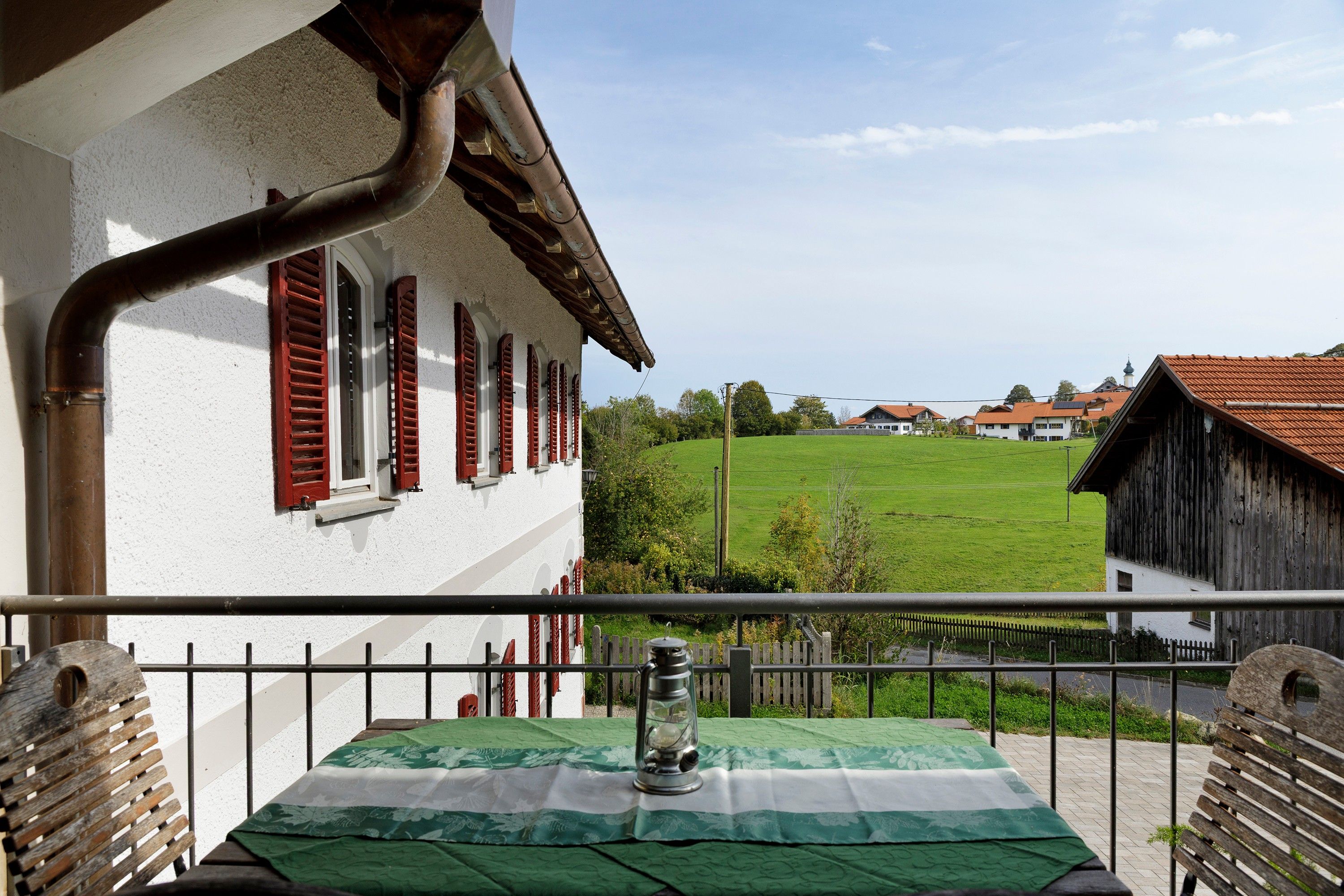 Ein Balkon mit Tisch, einer Laterne und Blick auf eine ländliche Landschaft mit Häusern und einem grünen Feld.