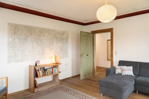 A living room with a bookshelf, a grey sofa, a wooden floor, a large abstract painting, and a green door. - Farmhouse 'Hohe Bleick' with Mountain View, Private Terrace and Wi-Fi (Wildsteig)