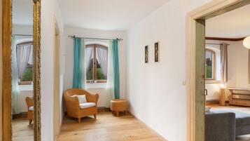 A room with a wicker chair, a small side table, and a grey sofa. There are two framed pictures on the wall.