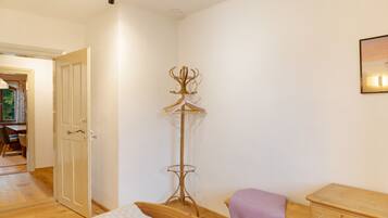 Quarto com cama, cómoda de madeira, cabideiro e porta que dá para outro espaço.