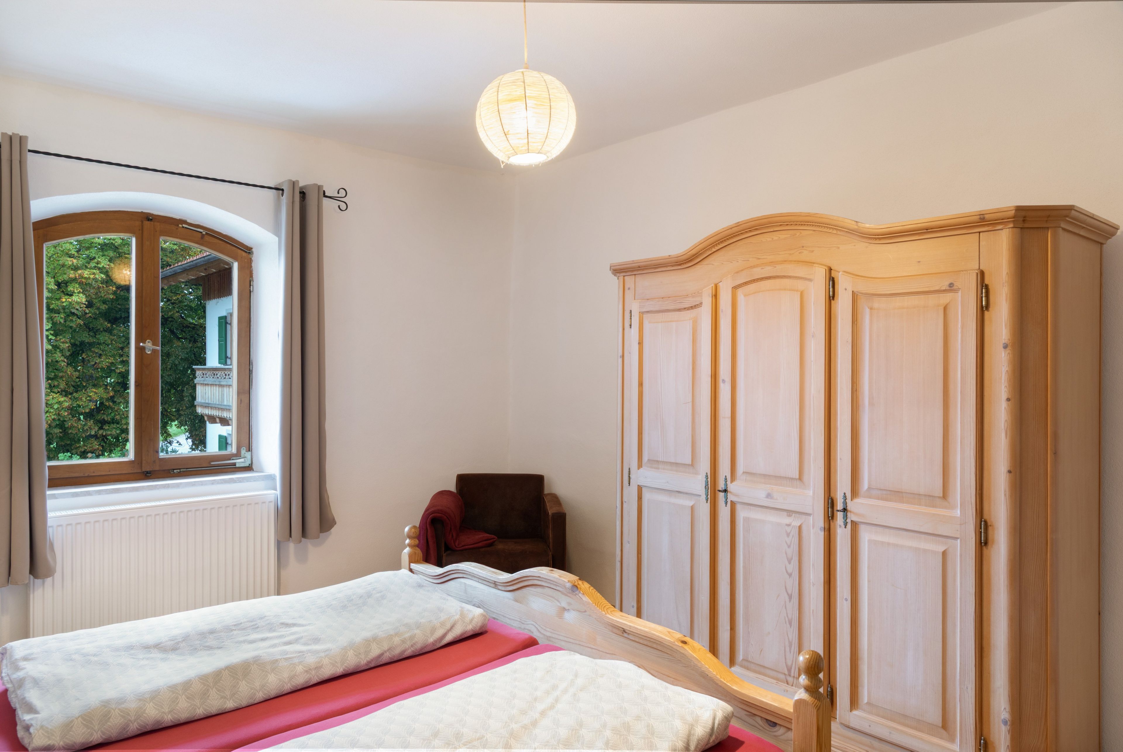 Een slaapkamer met een bed, een kledingkast, een raam en een hanglamp.