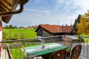 Un balcón con una mesa preparada para dos, con vista a un paisaje rural que incluye casas y un campo verde.