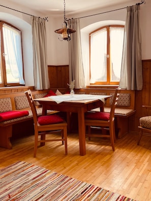 A dining area with a wooden table, chairs, and benches. There are windows with curtains, a hanging light fixture, and a patterned rug on the floor. - Farmhouse 'Niederbleick' with Mountain View, Shared Garden and Wi-Fi (Wildsteig)