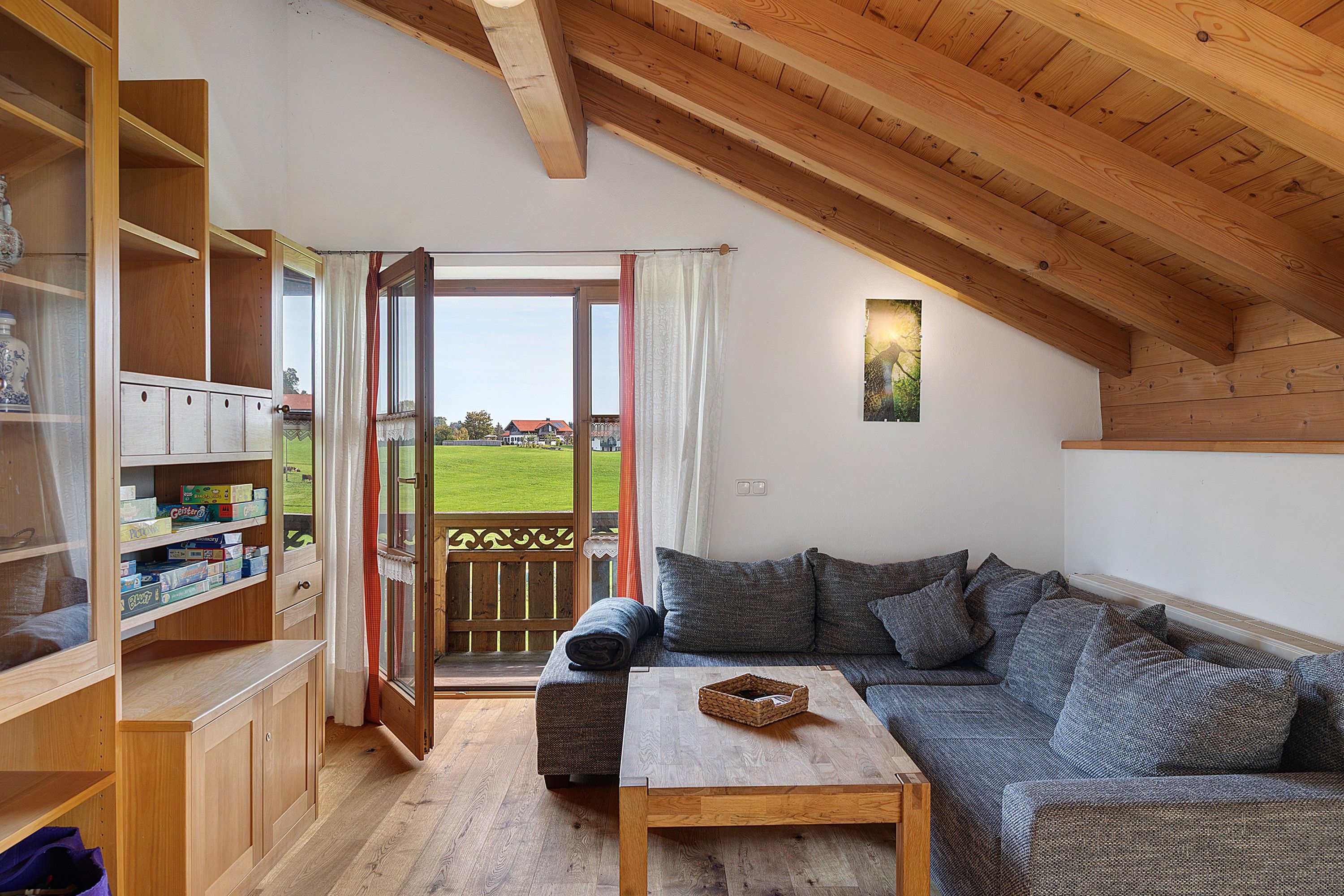 Een gezellige woonkamer met een houten plafond, een bank, een salontafel en uitzicht op een groen landschap door een glazen deur.