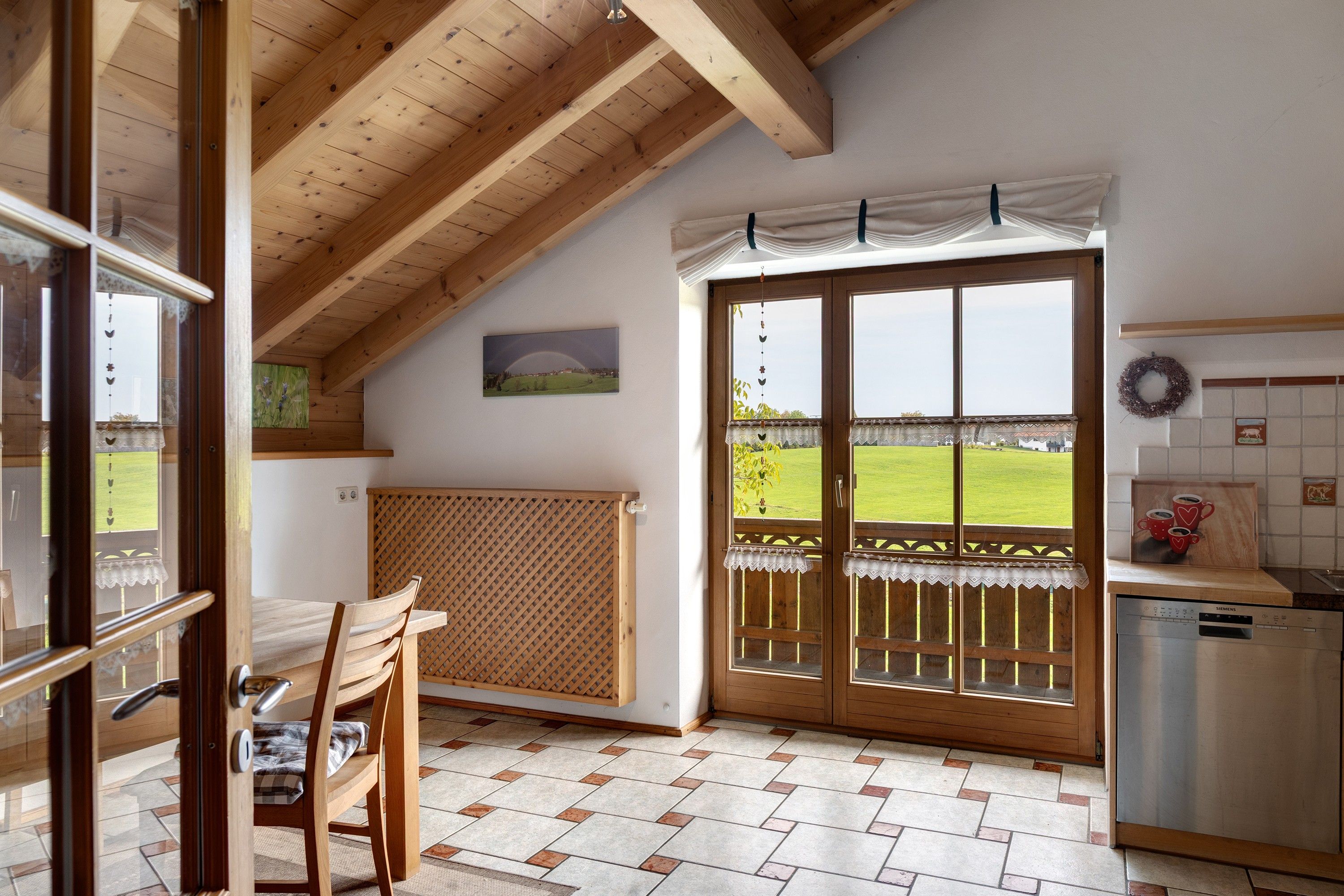 Eine Küche mit Blick auf ein grünes Feld, ein Holztisch mit Stühlen und eine Heizung.