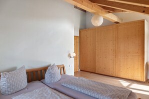 A bedroom with a bed, two pillows, a wooden wardrobe, and a wall-mounted light fixture.